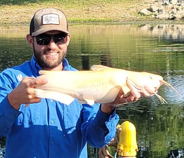 Large albino catfish being held by a happy fishman in blue with a baseball cap