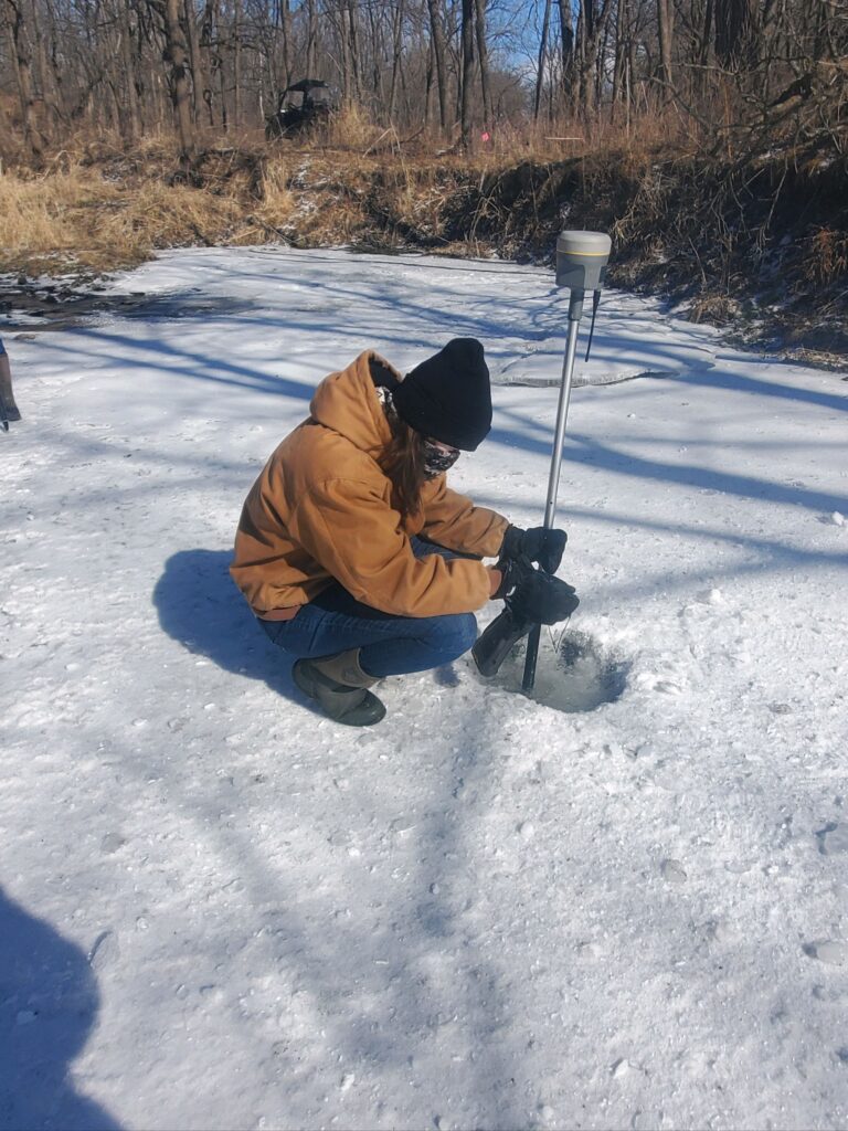 Katie Gisi using a GPS instrument in through a hole in the ice.