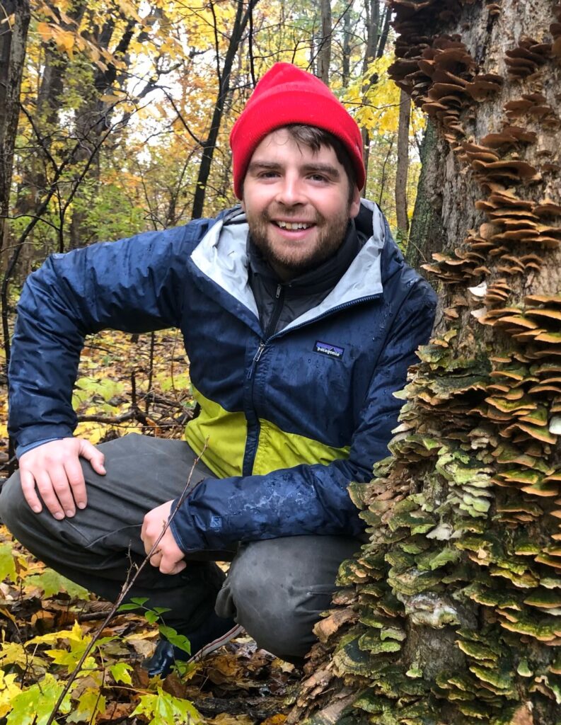 Lou in a red hat leaning next a tree with thousand of mushrooms