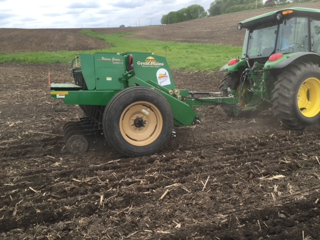 7 foot Great Plains drill being pulled by a John Deere green tractor in a bare field